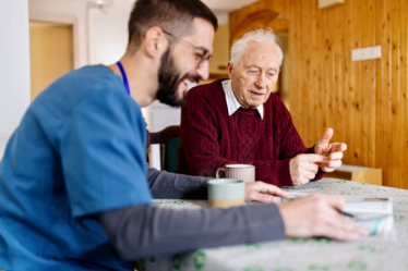 Gentlemen in a red cable knit jumper at a table with an NHS carer